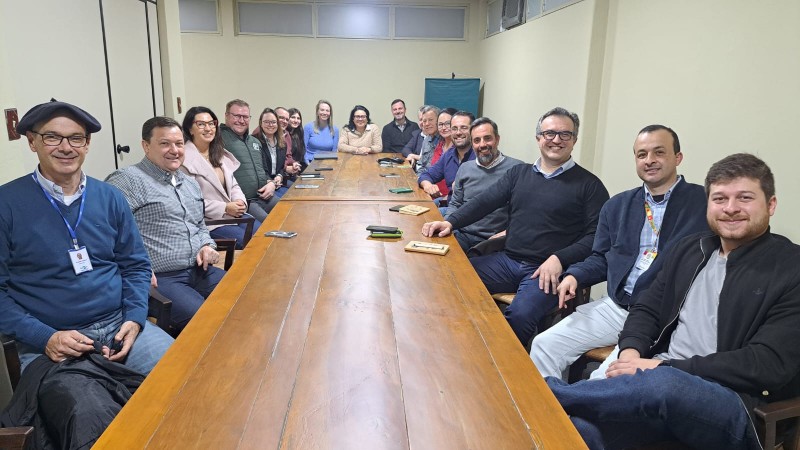 uma mesa de madeira encontra-se no meio da foto. ao redor, sorrindo, estão cerca de 20 pessoas, entre homens e mulheres, sorrindo para a câmera. o grupo fez parte da reunião que tratou sobre a descarbonização das cadeias produtivas do rio grande do sul.