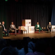 a imagem mostra o palco da associação médica do rio grande do sul. à esquerda, a secretária marjorie está em pé, em frente a um pulpito. sentados, autoridades que participam da conferência estadual do meio ambiente. ao centro ao fundo constam cubos com a marca da conferência.