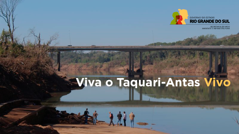 na imagem é possível ver uma ponte ao fundo, com o rio taquari em primeiro plano. abaixo da imagem tem pessoas observando o leito do rio. no centro o escrito Viva o Taquari-Antas Vivo. No canto superior direito, a logomarca do governo.