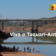 na imagem é possível ver uma ponte ao fundo, com o rio taquari em primeiro plano. abaixo da imagem tem pessoas observando o leito do rio. no centro o escrito Viva o Taquari-Antas Vivo. No canto superior direito, a logomarca do governo.