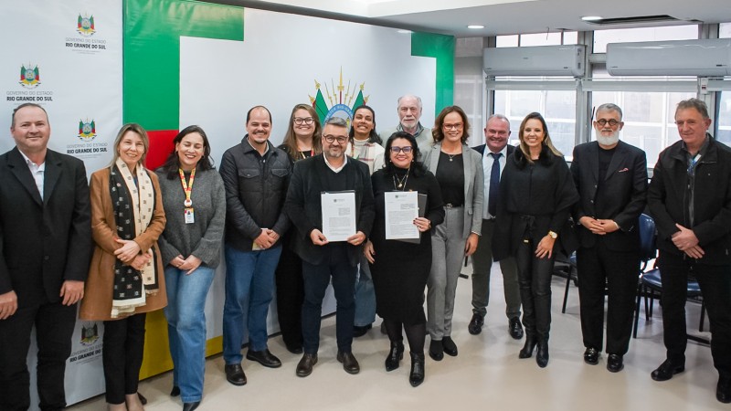 Secretária da Sema, Marjorie Kauffmann e secretário adjunto Marcelo Camardelli, em pé com o documento assinado em mãos, rodeados dos demais presentes na reunião.