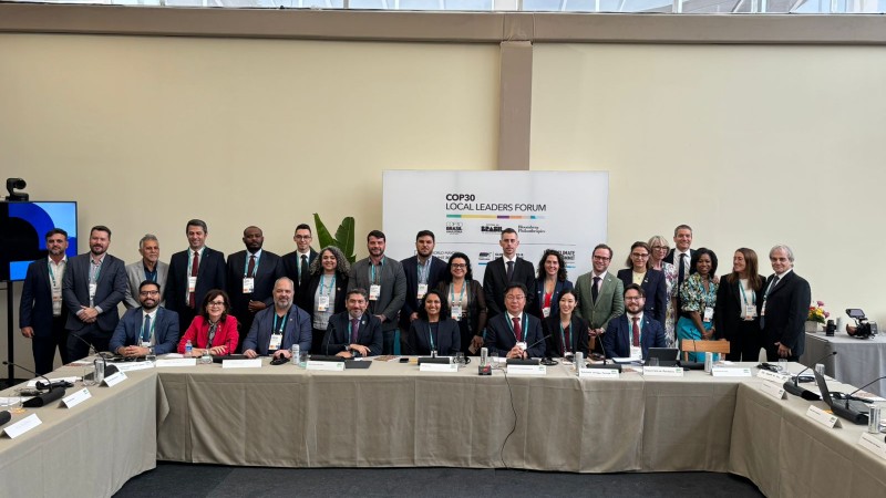 na imagem, l&iacute;deres locais est&atilde;o posicionados atr&aacute;s de uma mesa. todos sorriem para a c&acirc;mera.