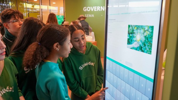 Estudantes utilizam totem interativo na Expointer. Uma das alunas est&aacute; clicando a tela.